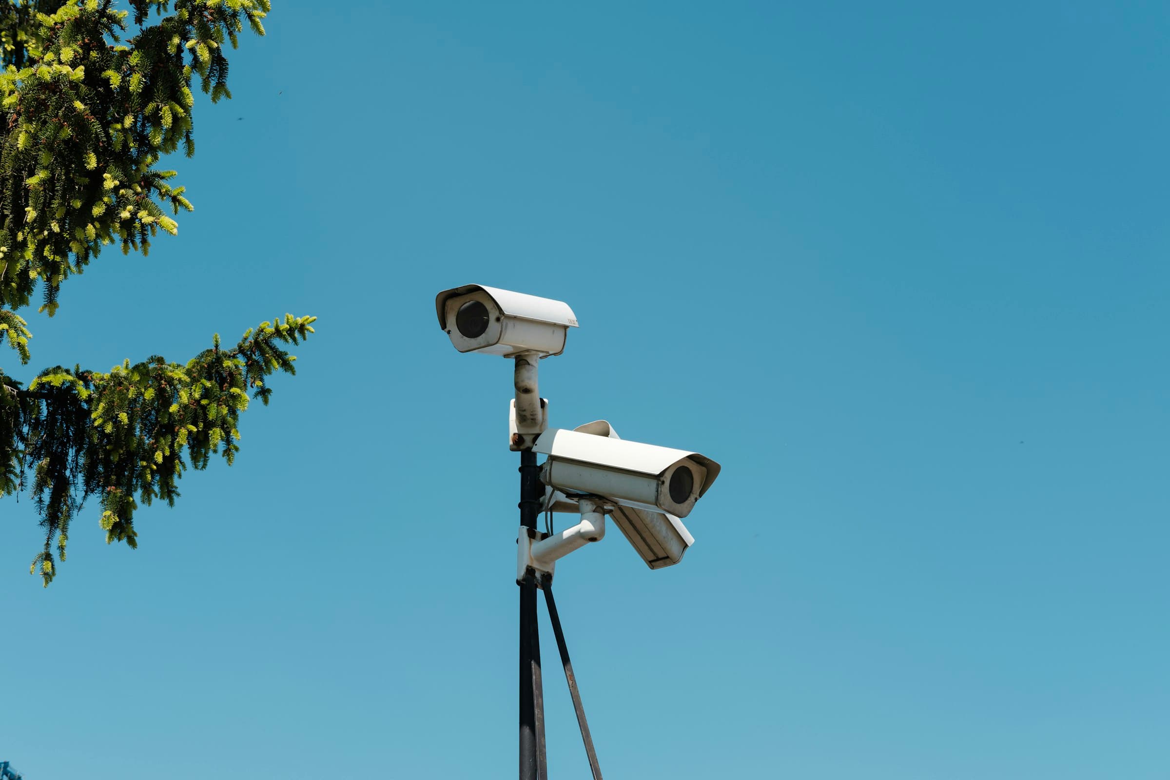 Two bullet cameras mounted on a pole bracket against open sky.