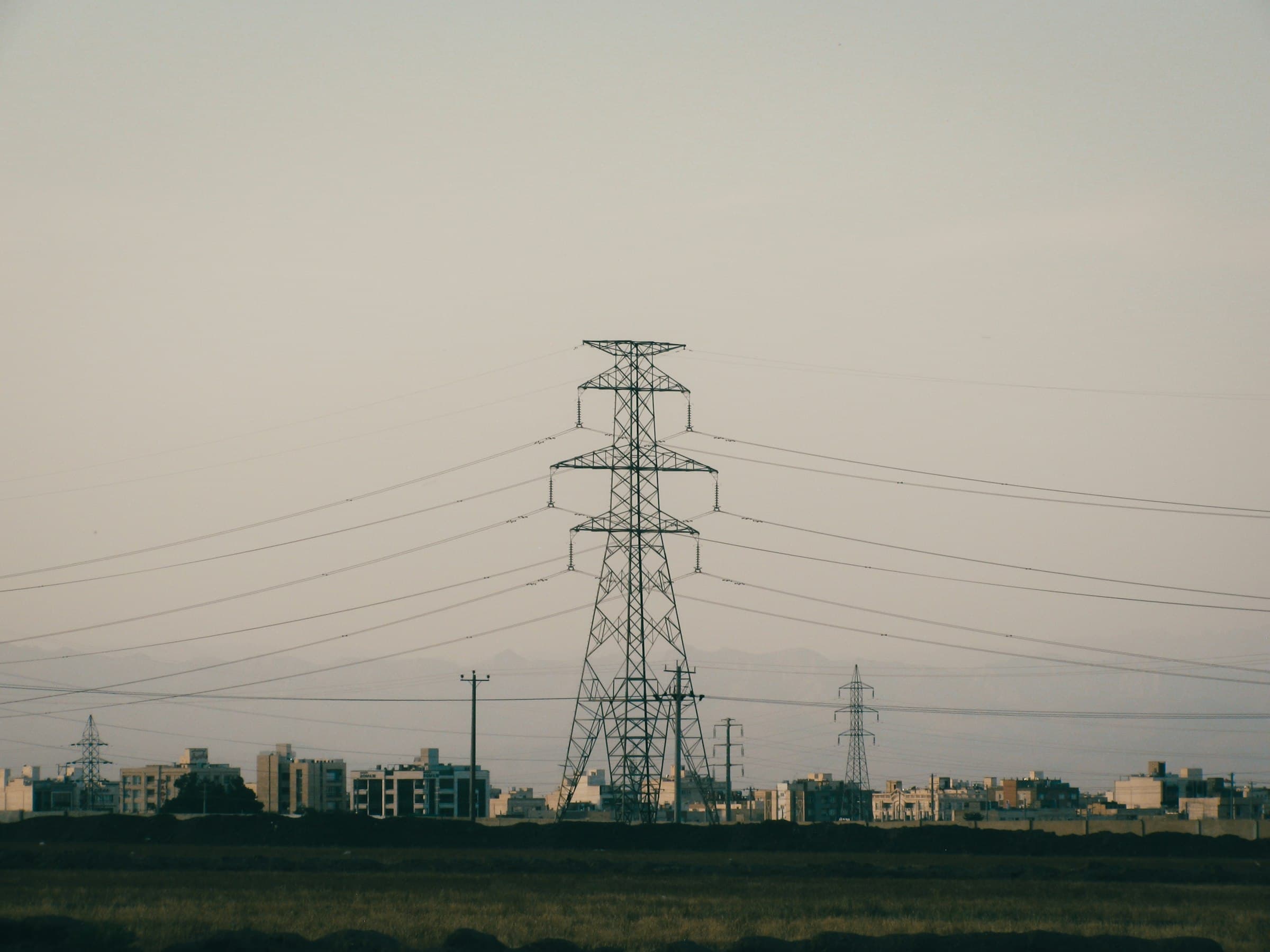 A lattice transmission pylon rising above a distant urban skyline.