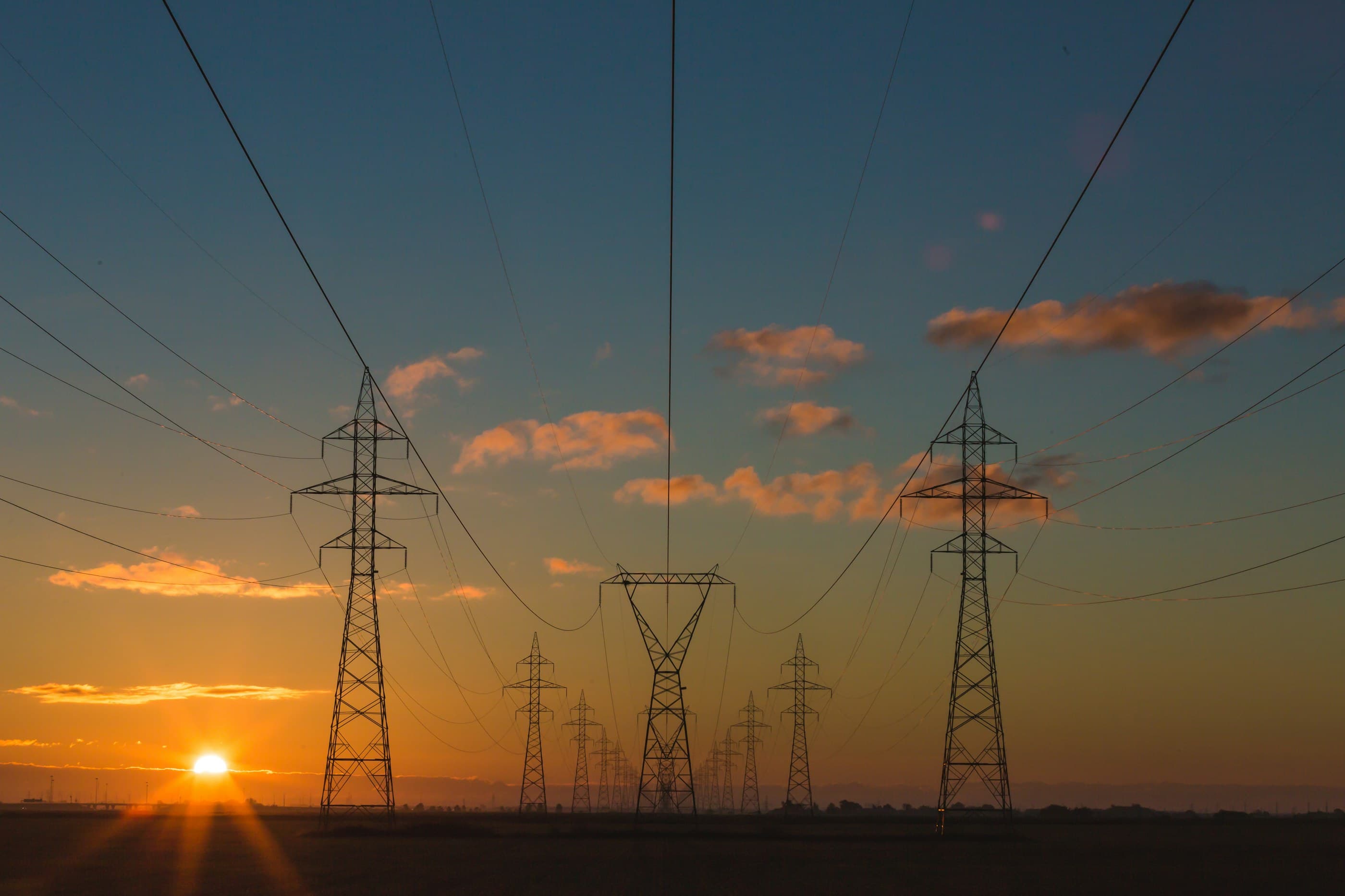 A high-voltage transmission corridor at dusk, silhouetted against a sky running from deep blue through magenta to a narrow band of amber at the horizon.