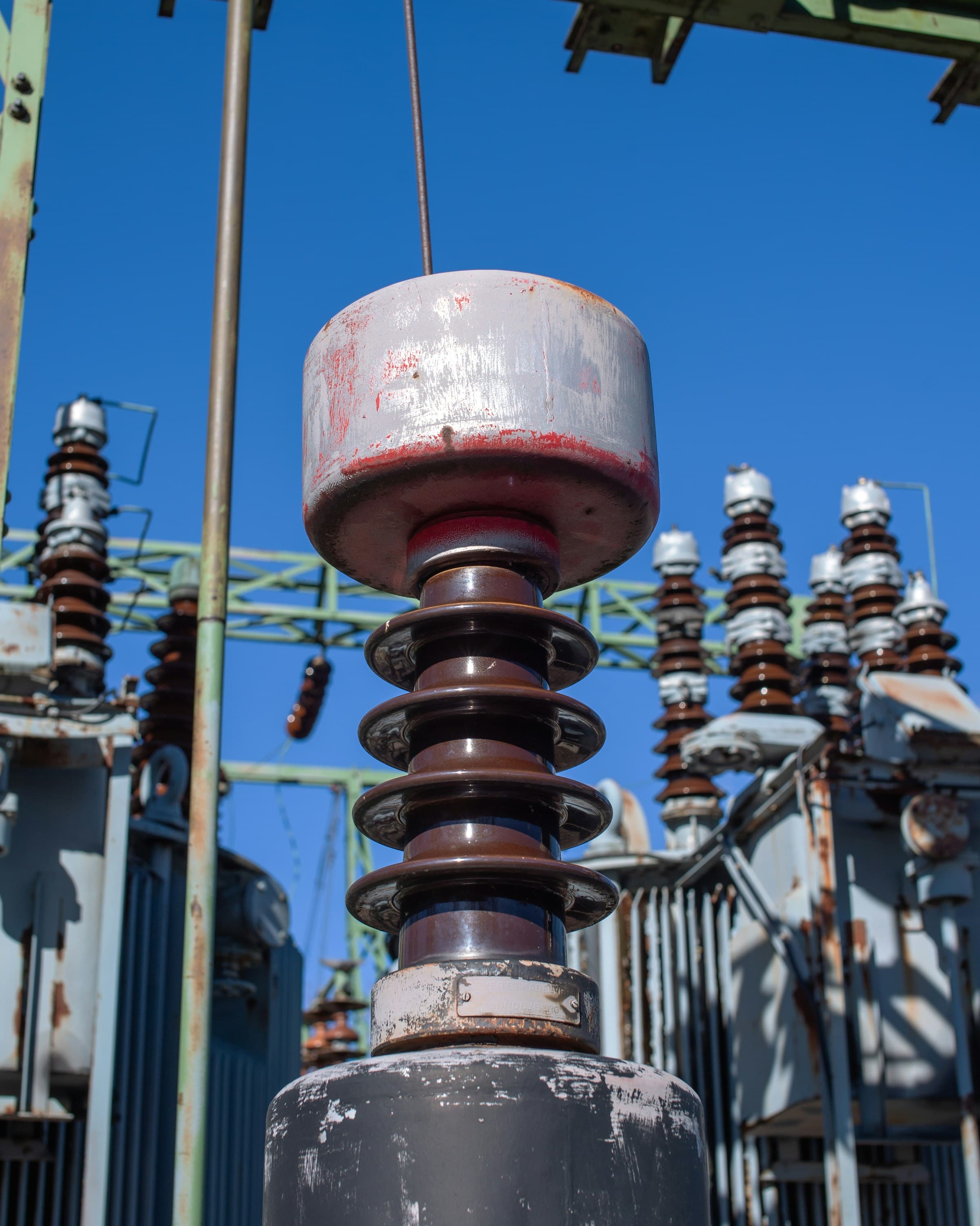 Close view of a high-voltage insulator stack and bushing, ribbed sheds stacked vertically against the sky.